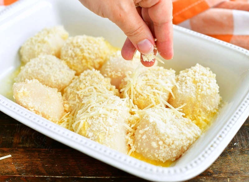 sprinkling Panko covered scallops in a pan with some grated parmesan cheese