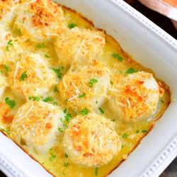 top view of baked scallops in a white baking dish with brown checkered towel next to it