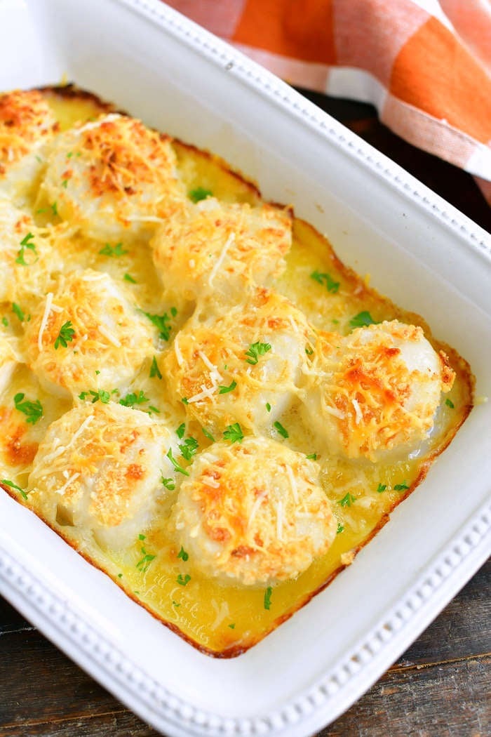 top view of baked scallops in a white baking dish with brown checkered towel next to it