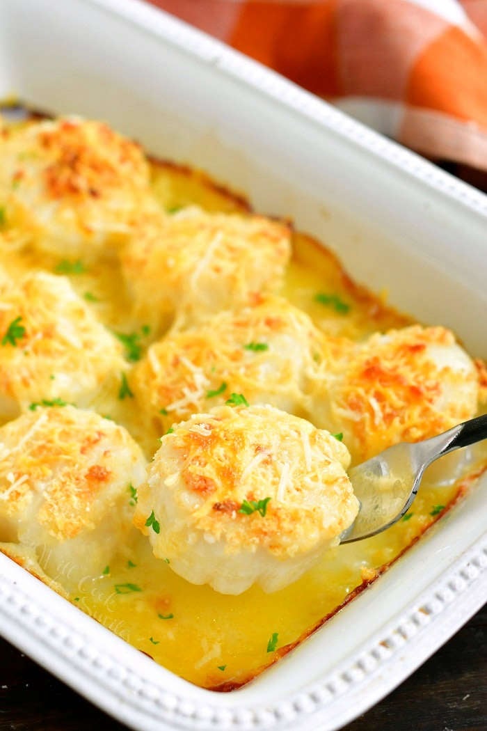 picking up one baked scallop with a fork out of the baking dish