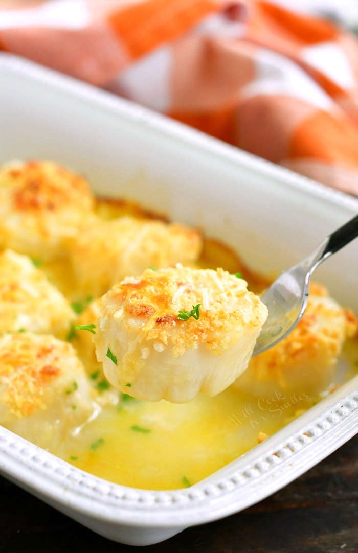 holding one scallop on the fork with the dish of scallops on the background