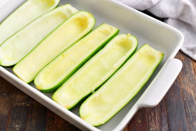 hollowed out zucchini halves paid side by side in a baking dish