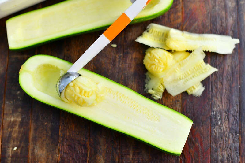 scooping the center out of zucchini half with a melon baller
