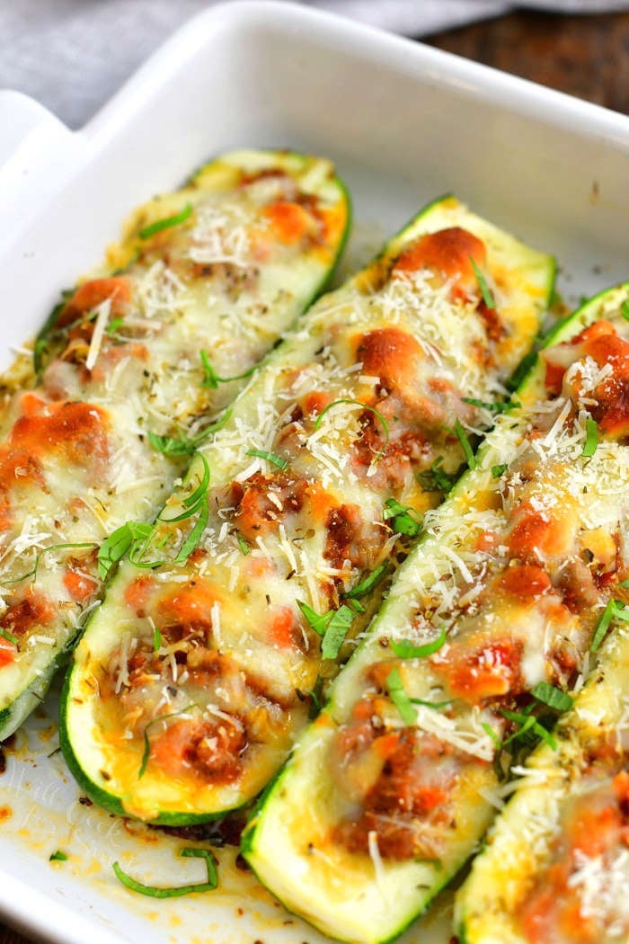 closer view of baked zucchini boats in a white baking pan topped with minced basil and shredded Parmesan