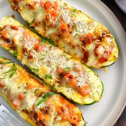 three stuffed baked zucchini boats side by side on a light tan dish with a grey towel next to it