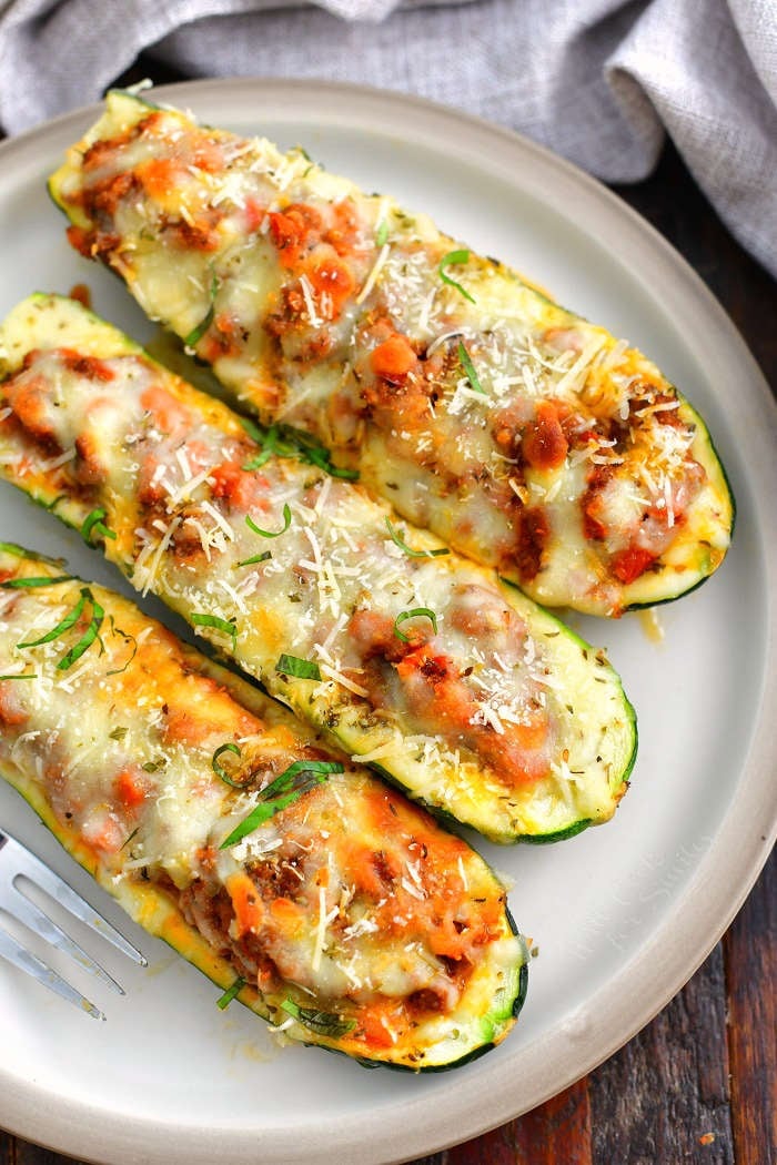 three stuffed baked zucchini boats side by side on a light tan dish with a grey towel next to it