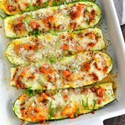 several stuffed zucchini halves side by side baked in a white baking dish and topped with minced basil and shredded parmesan