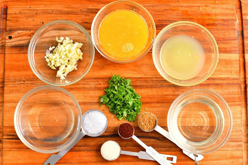 ingredients for steak marinade in small glass bowls in the cutting board and seasoning ingredients in measuring spoons with minced cilantro in the center