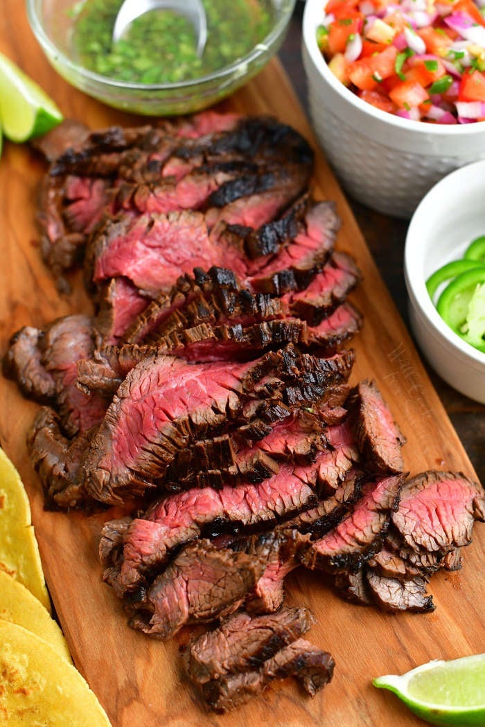 sliced grilled steak on a cutting board with taco toppings visible around