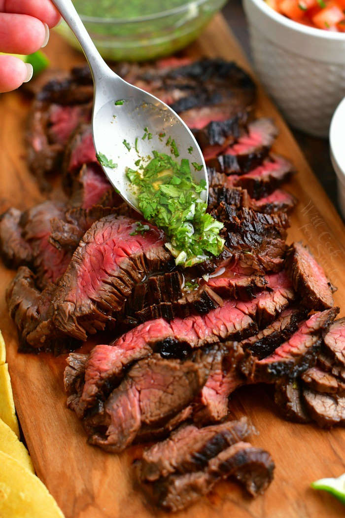 spooning cilantro lime topping over the sliced steak on the cutting board