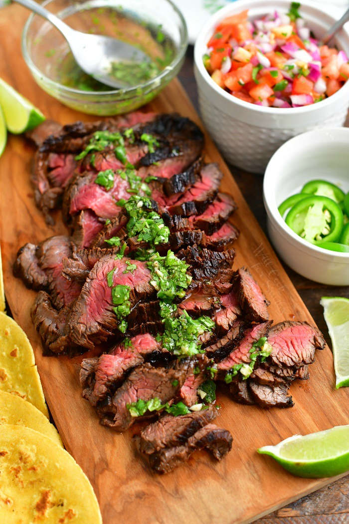 sliced steak on a cutting board topped with cilantro topping along the center and toppings around the cutting board