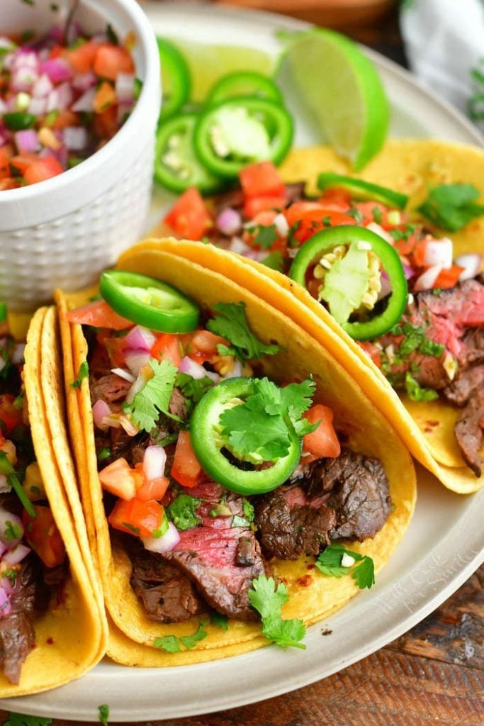 closer view of steak taco in a plate topped with jalapeno rings, pico, and cilantro