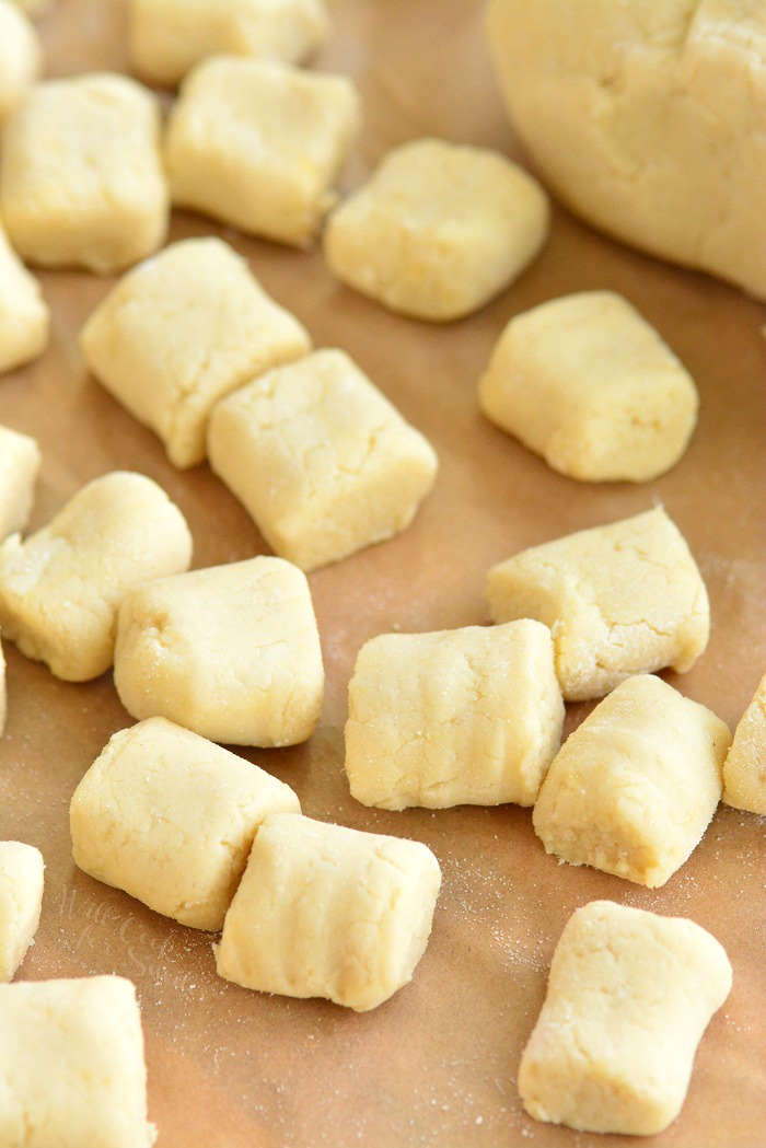 close up view of cut and rolled uncooked gnocchi spread out on a sheet on parchment paper