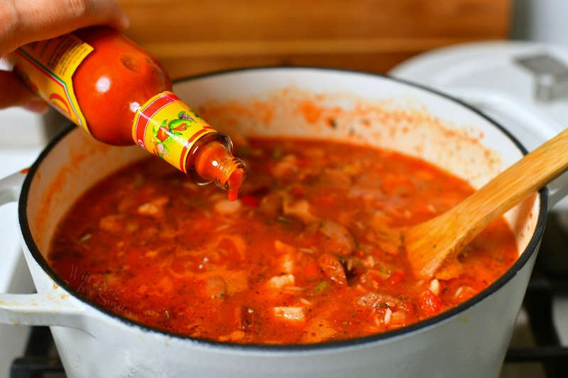 adding a few drops of hot sauce into the pot of jambalaya while it's cooking on the stove