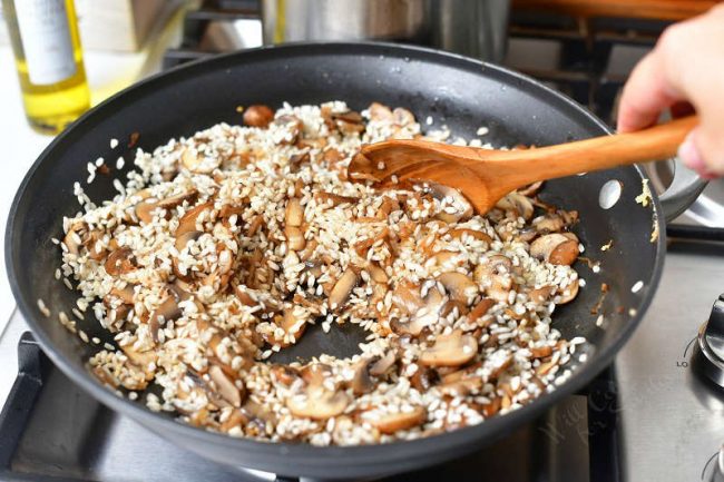 woman's hand stirring risotto rice with wooden spoon