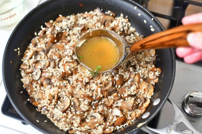 overhead photo: adding broth to a skillet of rice and mushrooms for a mushroom risotto recipe