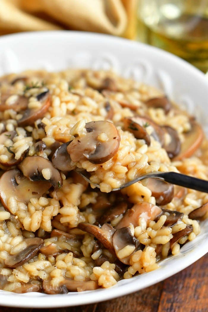 close up photo of arborio rice with mushrooms on a spoon in white serving bowl