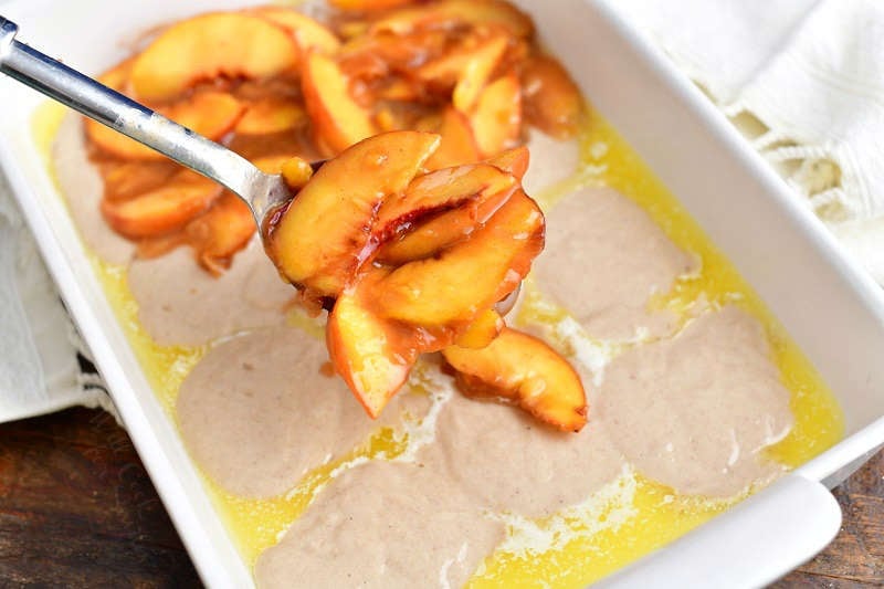 spooning peaches over the batter and butter in a baking pan