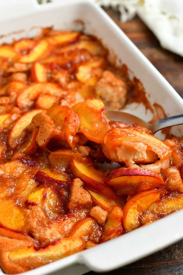 starting to scoop peach cobbler out of the white baking dish using a metal spoon