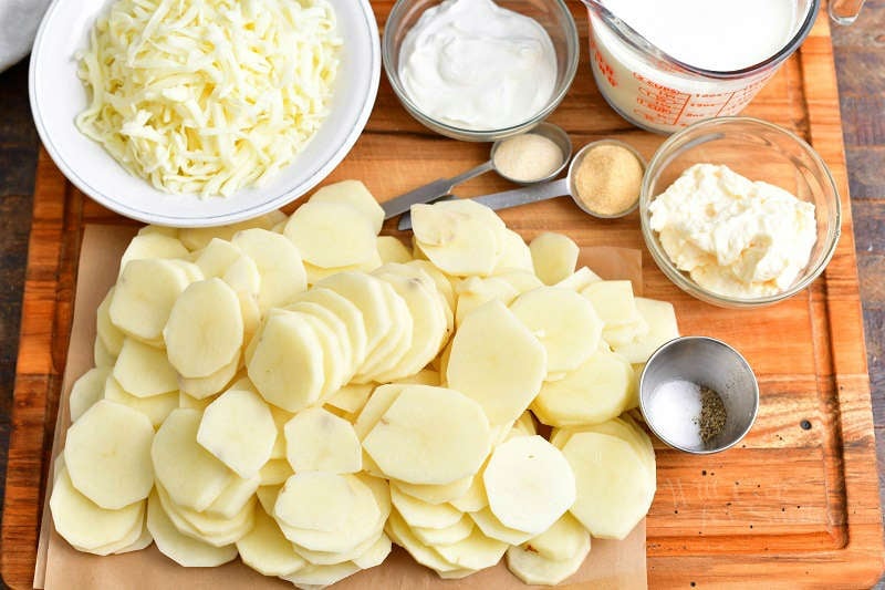 sliced potatoes, shredded cheese, sour cream, mayo, cream and other ingredients on cutting board