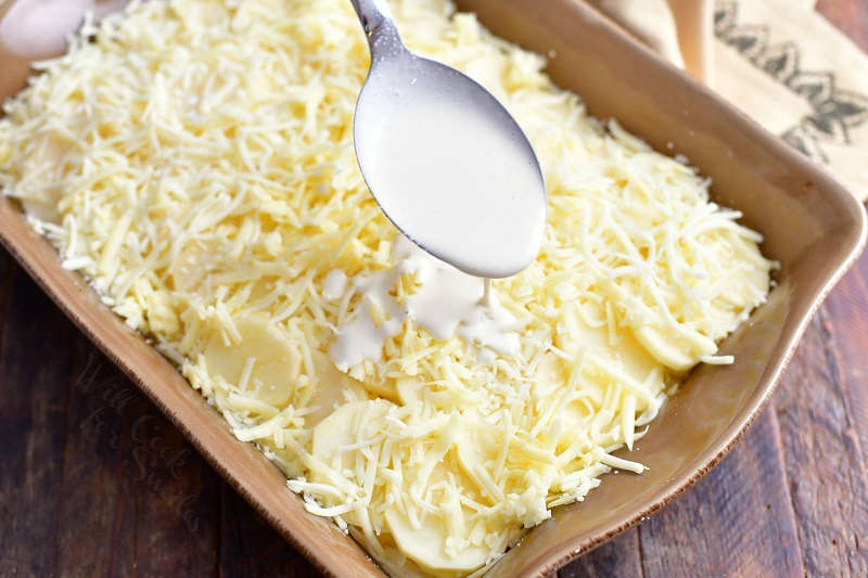 white cream sauce being spooned over shredded white cheese