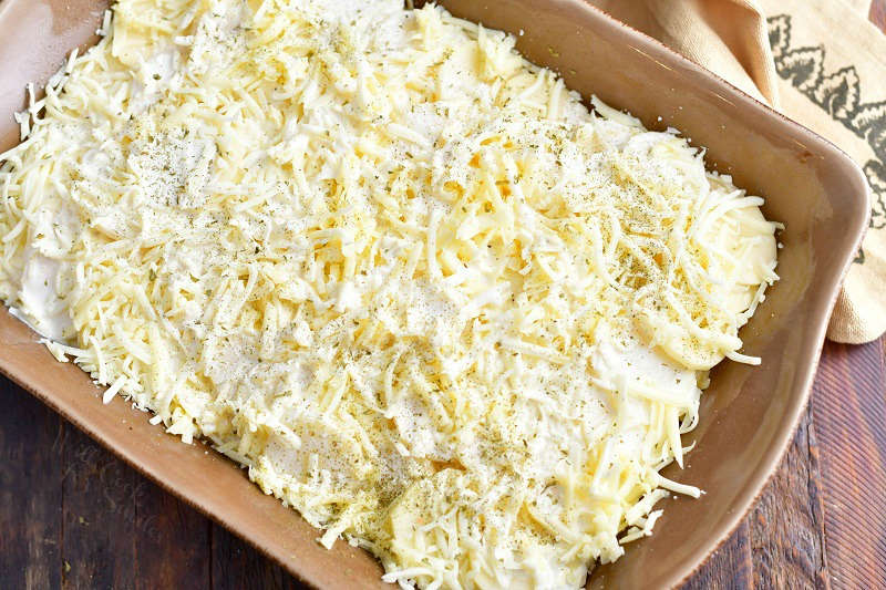 shredded cheese on sliced potatoes in baking dish for a scalloped potatoes recipe