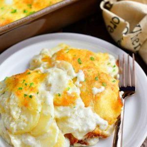 serving of creamy scalloped potatoes on small round white plate with a fork. Remaining casserole in background