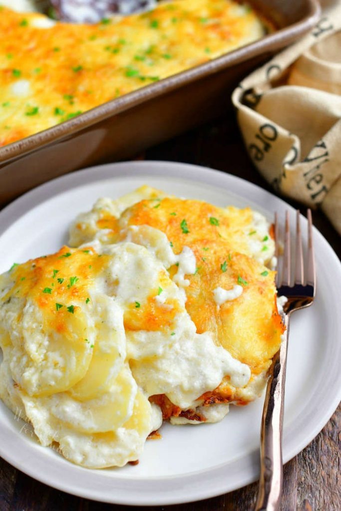 serving of creamy scalloped potatoes on small round white plate with a fork. Remaining casserole in background