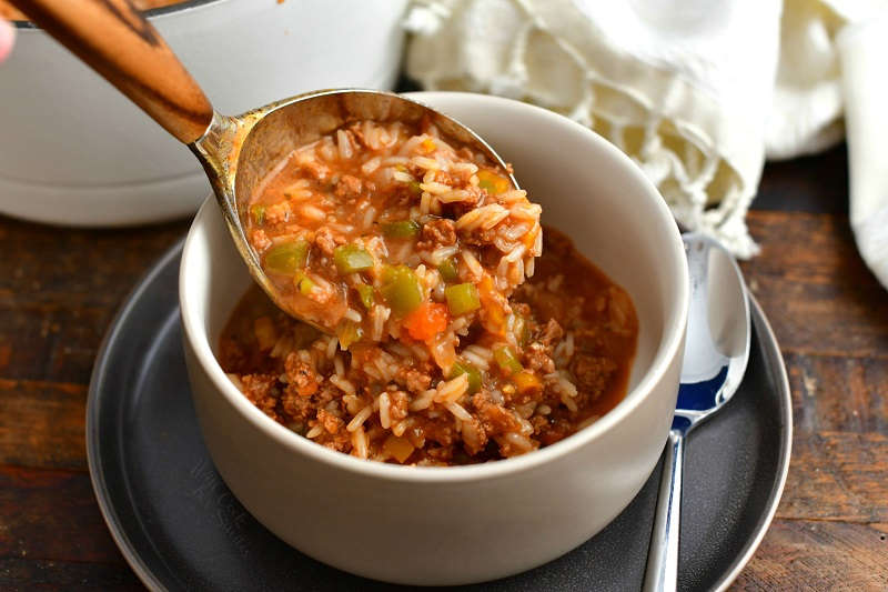 ladling beefy rice soup into a white bowl