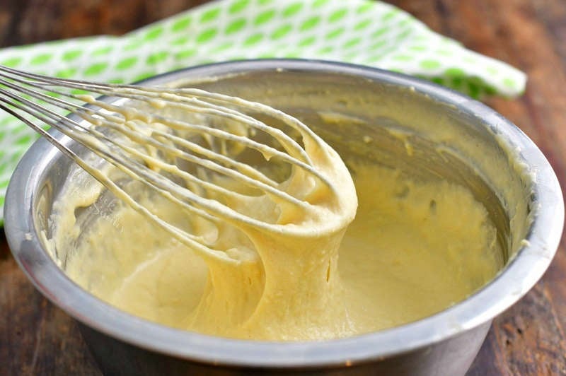 whisk pulling some pancake batter out of the mixing bowl and a green leaf towel behind the bowl