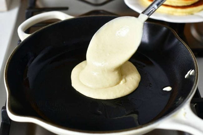 pouring pancake batter into a cooking pan with a metal ladle
