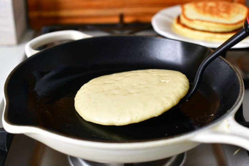 starting to flip a pancake with a spatula in a cooking pan and as stack of two pancakes on the background