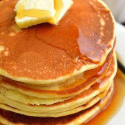 top view of the stack of pancakes topped with 2 slices of butter and maple syrup