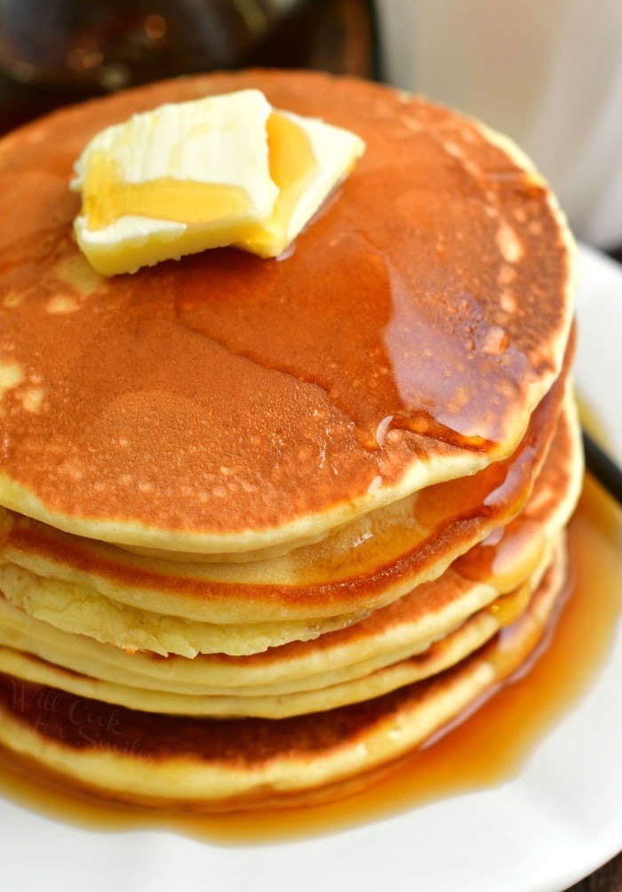 top view of the stack of pancakes topped with 2 slices of butter and maple syrup