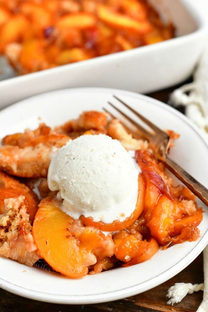 peach cobbler in a white bowl topped with a scoop of vanilla ice cream and a fork on the side of the bowl