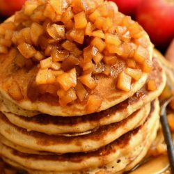 side view of large stack of pancakes topped with apple pie topping on a bowl plate