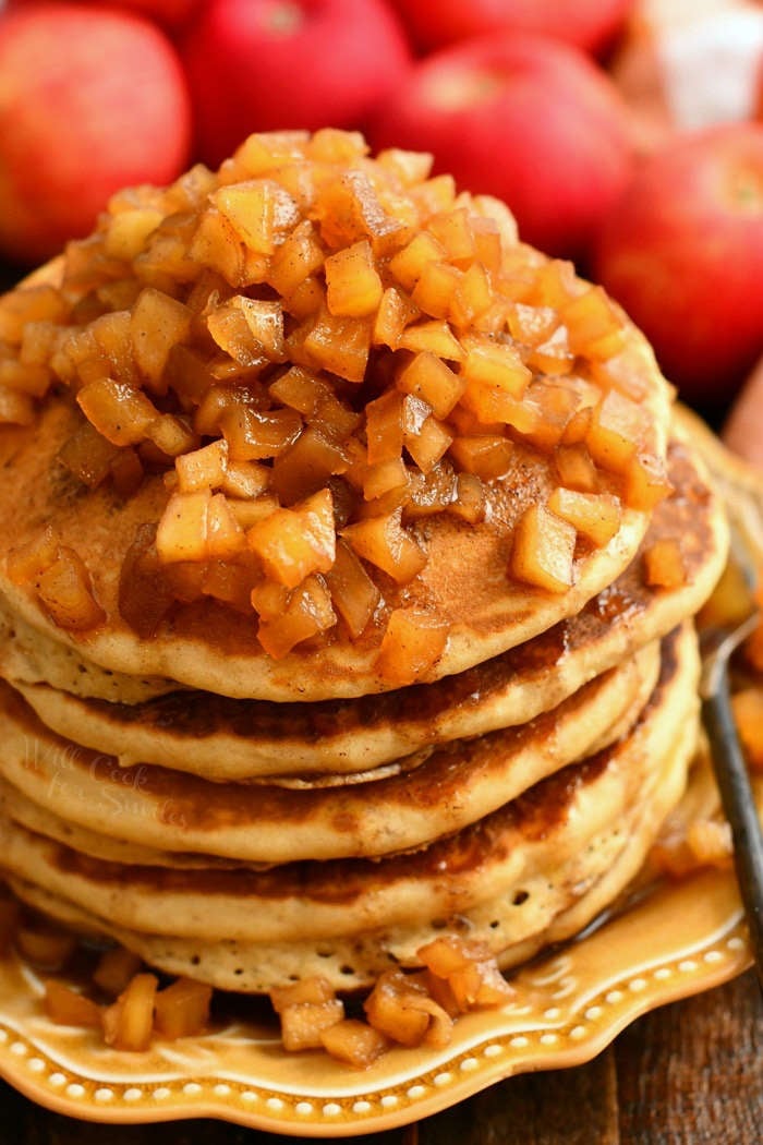 side view of large stack of pancakes topped with apple pie topping on a bowl plate