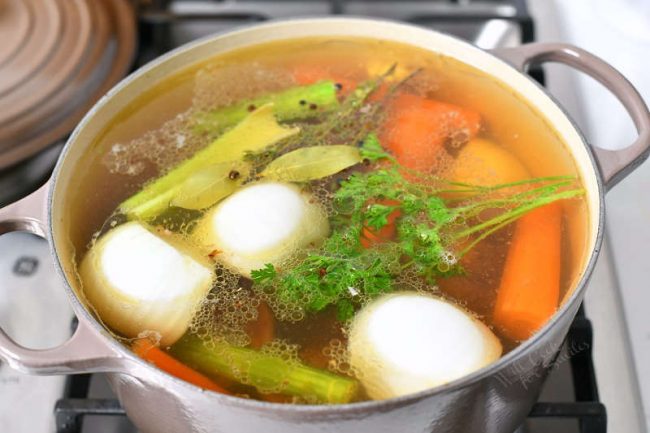 pot with vegetables and other ingredients to make homemade stock in large white pot