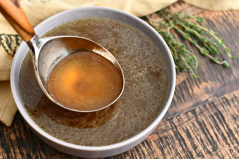 overhead photo: golden brown beef stock on ladle over bowl filled with the stock