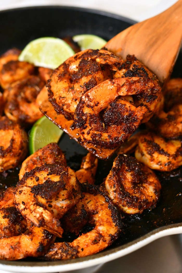 cooked blackened shrimp in pan with one on wooden spoon above pan