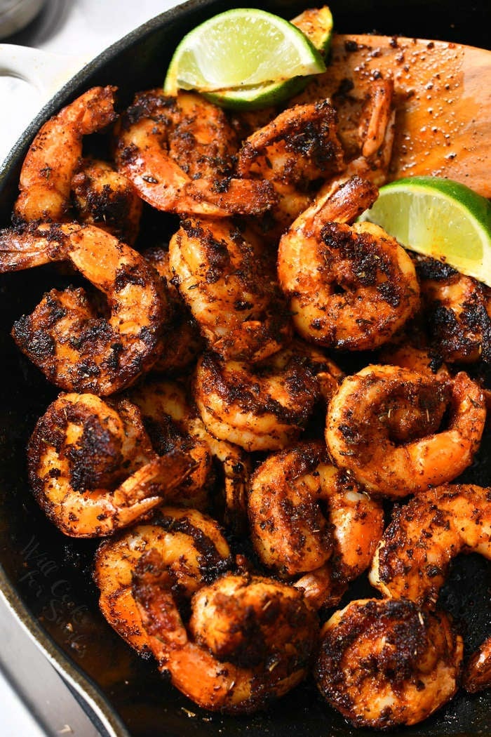 overhead photo: spicy tail-on shrimp in black cast iron pan with lime wedges