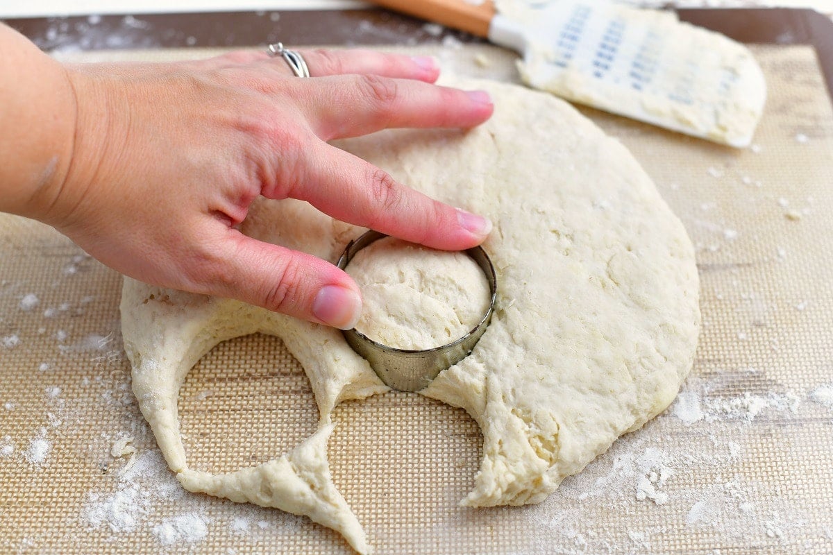 woman's hand pressing round metal cutter into circle of biscuit dough
