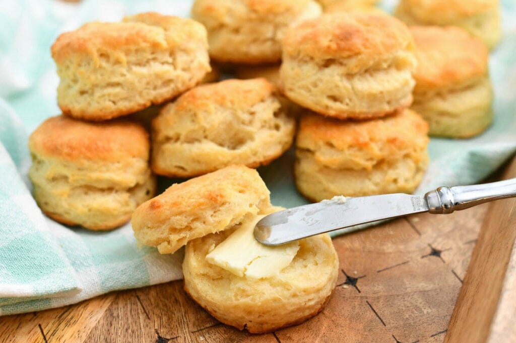knife schmearing butter onto a warm biscuit - stack of them behind it