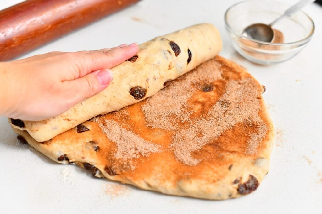woman's hand rolling bread dough with cinnamon sugar mixture