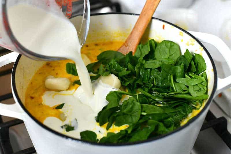 pouring heavy cream into white Dutch oven with fresh spinach