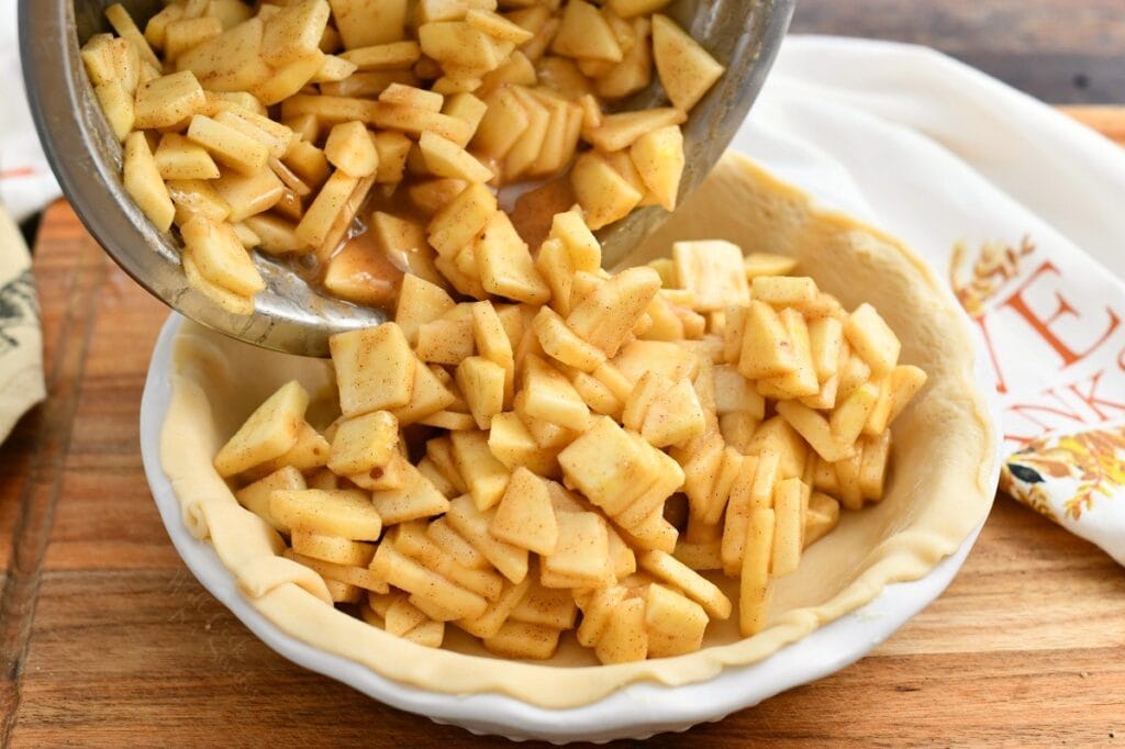 pouring spiced apple mixture into unbaked pie crust