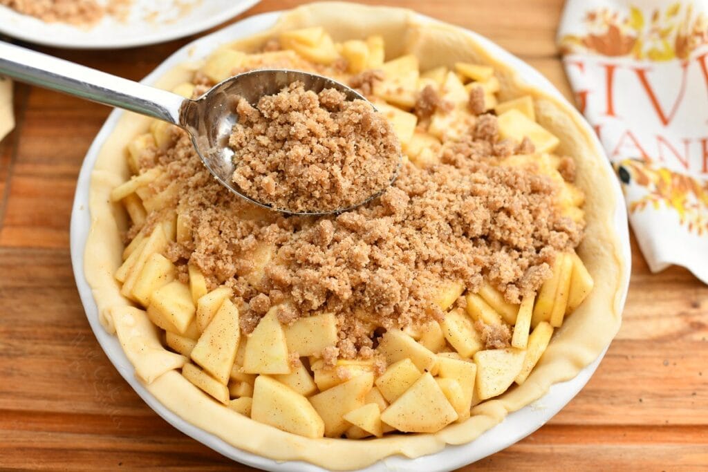 using spoon to add streusel topping for apple pie