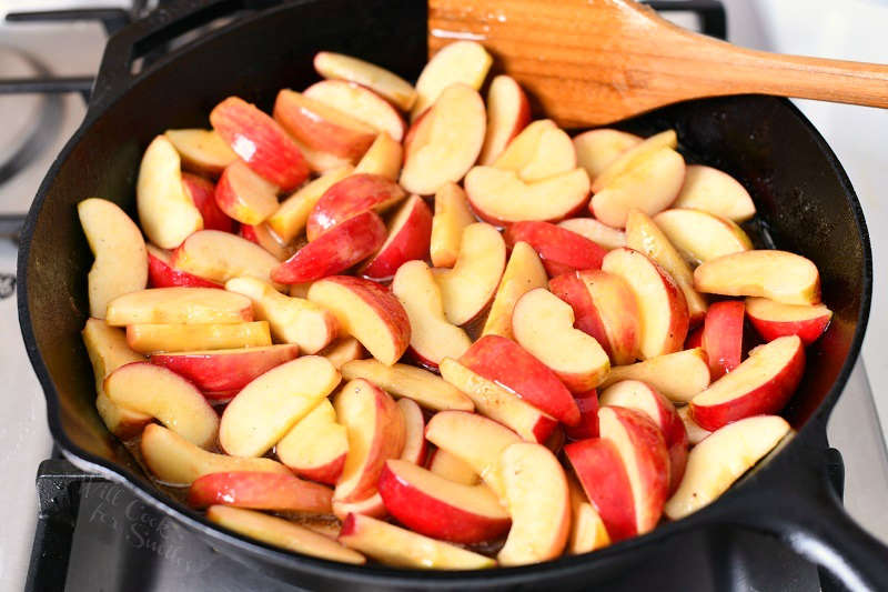 fresh red apple slices in black skillet with wooden spoon for fried apples recipe