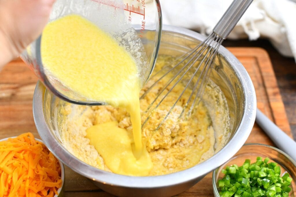 adding eggs to cornmeal flour in stainless steel mixing bowl