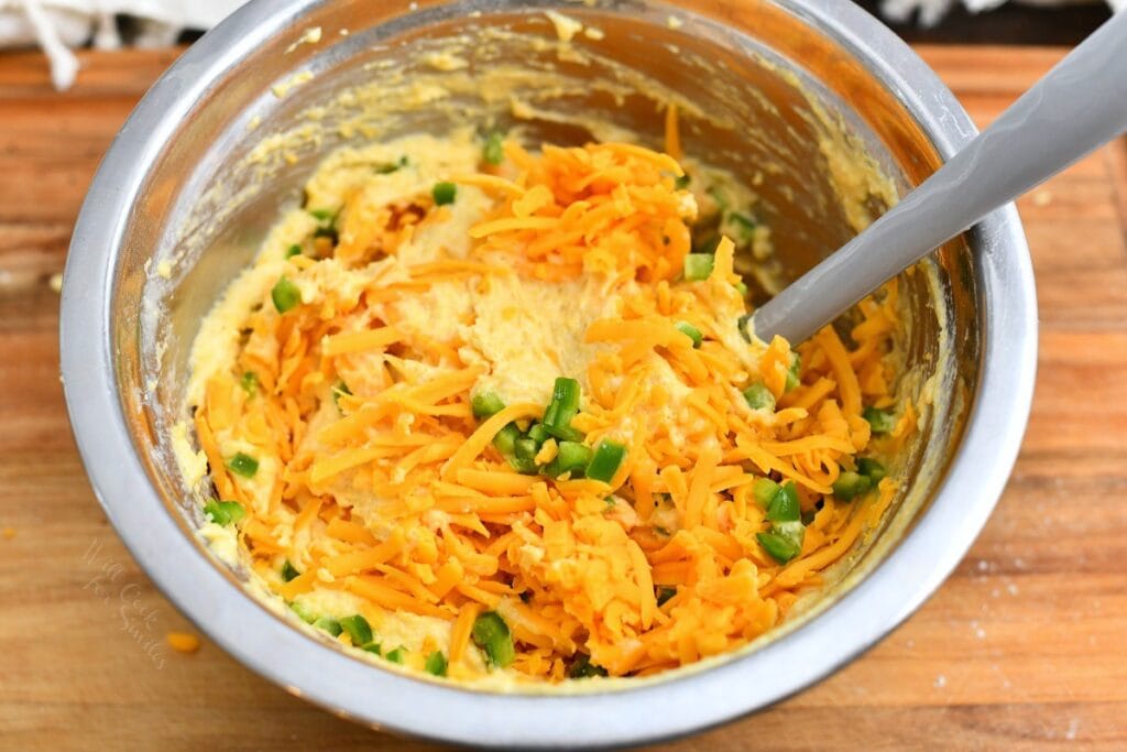 mixing shredded cheddar cheese and jalapenos into cornmeal batter in stainless steel mixing bowl